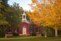 Front exterior of old traditional red brick schoolhouse building during autumn 