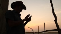silhouette of a cowboy dialing on a cellphone 