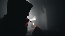 Silhouette of young teenage man or teenage boy sitting on his bed lighting and smoking a cigarette or doing drugs.