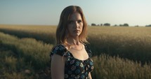 Portrait of young woman in green grass in summer nature in sunset during golden hour in slow motion.