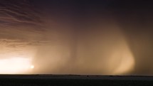 A bright Colorful Sunset Behind Heavy Bands Of Rain With Lightning Striking The Ground.