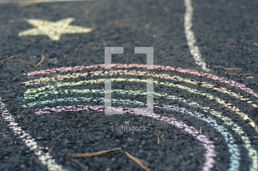 Chalk drawings of a rainbow and star on a concrete driveway.