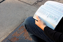 a man sitting on a bench outdoors reading a Bible 