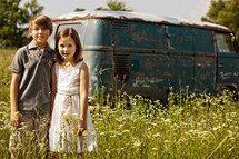 brother and sister in front of an old van in a field