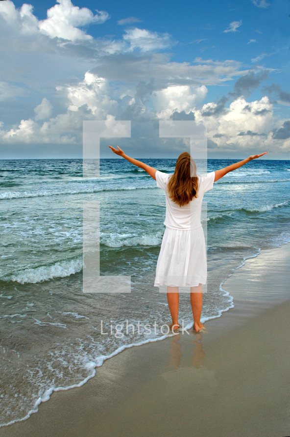 woman standing on a beach with raised hands 