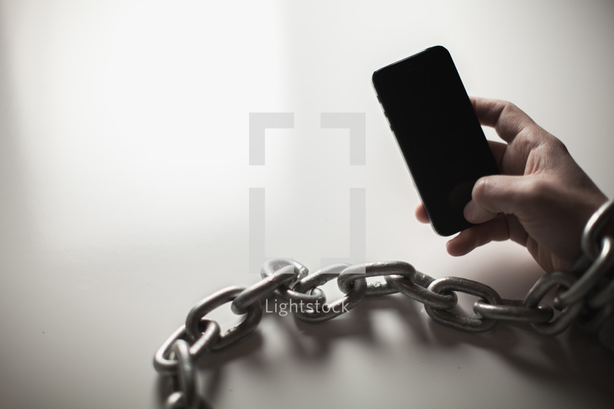 Wrist bound with chain holding a cell phone.