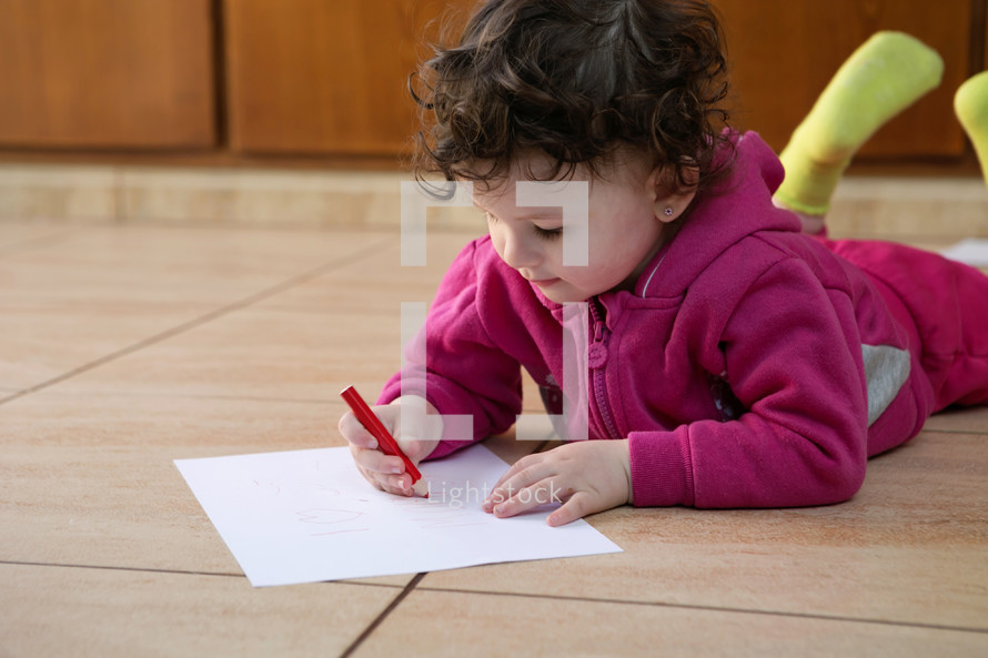 a child drawing on paper on the floor 
