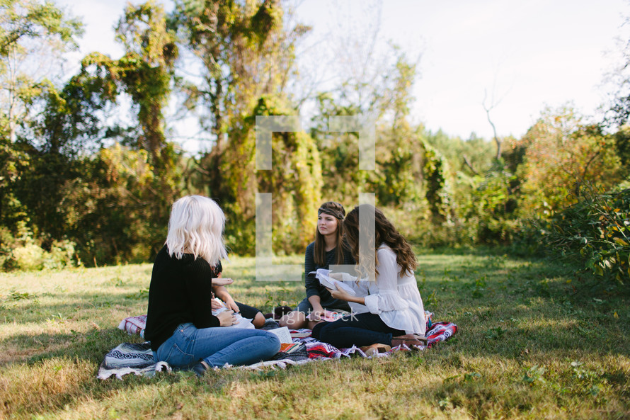 young women reading Bibles on a blanket outdoors 