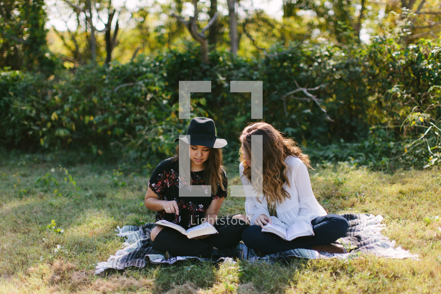 young women sitting on a blanket outdoors reading Bibles 