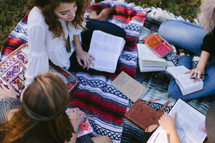 young women reading Bibles on a blanket outdoors 
