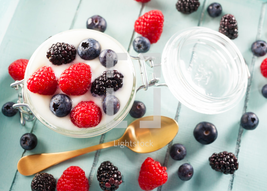 Jar of yogurt and berries on a light blue wooden tray