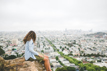 a woman sitting on a rock looking out at San Francisco suburbs 