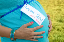 pregnant woman with her hands over her belly with a tag - from god with love