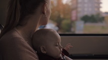 Mother with baby daughter traveling. Woman holding child on the lap and looking out the window