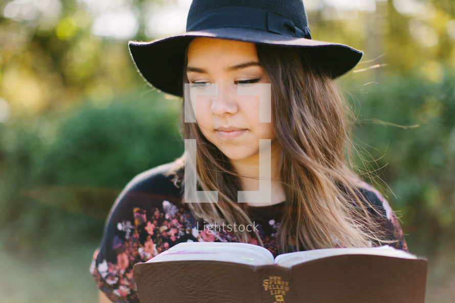 teen girl in a hat reading a Bible 