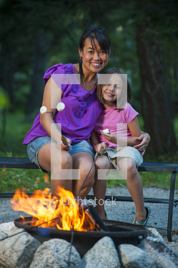 mother and daughter roasting marshmallows over a fire 