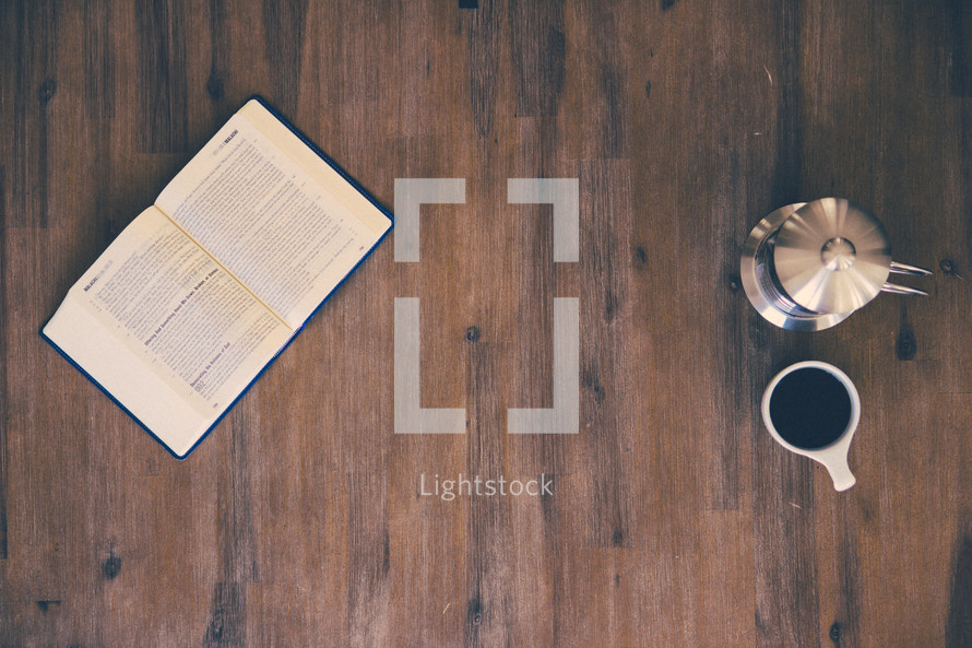 open Bible, coffee mug, and coffee pot on a wood floor 