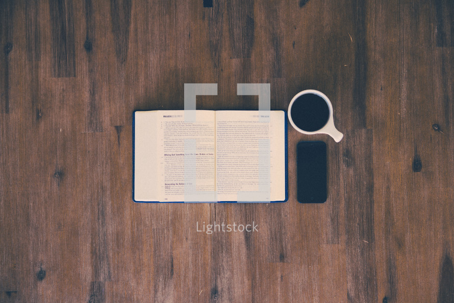 open Bible, cellphone, and coffee mug on a wood floor