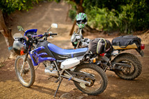 Motorcycles with helmets parked in the dirt.