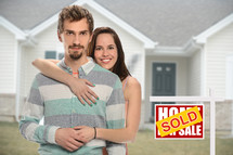 couple standing beside a sold sign in front of their new home 