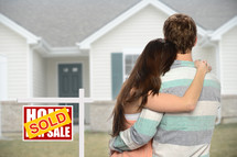 couple standing next to a sold sign in front of their new home