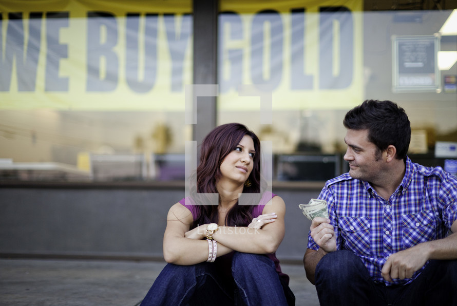 man holding out cash to a woman in front of a we buy gold store