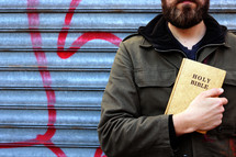 a man standing in front of metal garage doors with graffiti on them holding a Holy Bible 