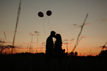 Couple kissing at sunset near floating balloons