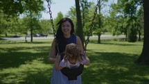 a mother pushing a toddler on a swing 