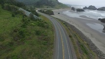 Aerial view of a car driving on a highway alongside the ocean shore.