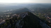 Aerial shot of drone panning right around Mount Titano, in San Marino, with a sunset in the background.