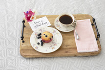 breakfast in bed, blueberry muffin, coffee, and flowers on a wooden tray 