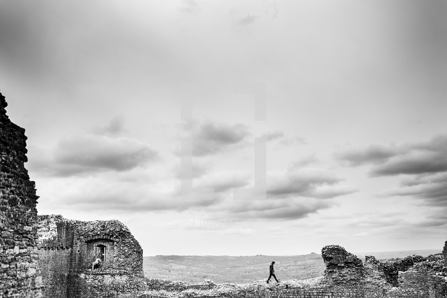man walking on remaining walls at a ruins site  