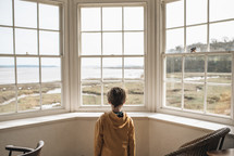child looking out a window at a beach 
