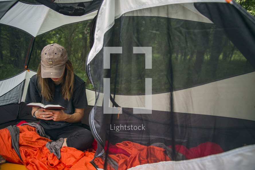 A woman sitting in a camping tent and reading the Bible.