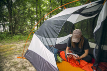 A young woman sitting in a camping tent while reading the Bible.