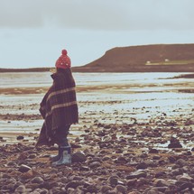 a girl child wrapped in a blanket on a shore 