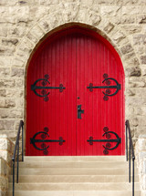 stone wall frames arched red door with decorative metalwork