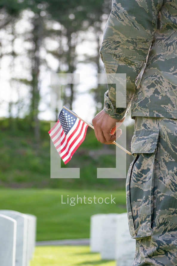 soldier holding an American flag standing in a cemetery 