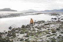a woman in a coat walking along a muddy shore in Alaska