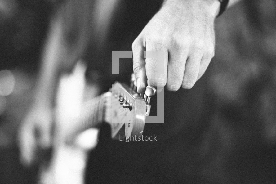 a man turning guitar pegs tuning his guitar 