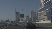 Busy rush hour traffic as people drive in cars to work with distant Dubai skyline and buildings in middle east.