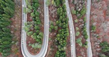 Aerial, tilt up, drone shot, of a cars driving on hairpins, on a winding, hillside road, in Romanian forest, on a mountain, on a sunny, fall day, in Romania