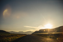 A road leading toward mountains and a sunset.