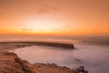 sea wall and tide washing onto a beach at sunset 