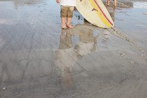 Feet of a young person and the bottom of a surfboard, both in shallow water