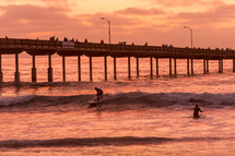 surfer surfing near a pier at sunset 
