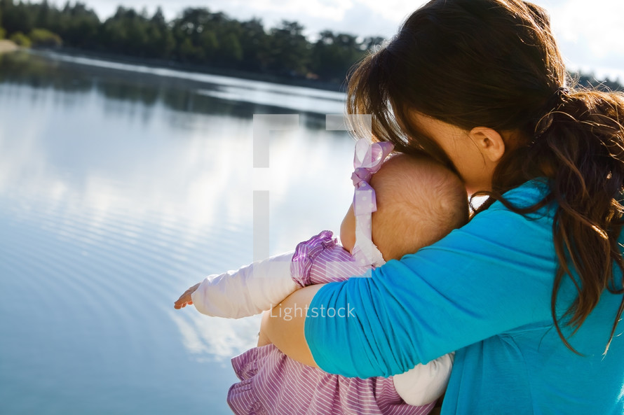 mom hugging baby daughter by a lake