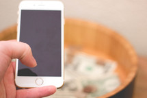 woman holding an iPhone above a bowl of money 