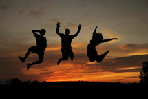 A silhouette of three people jumping into the air.